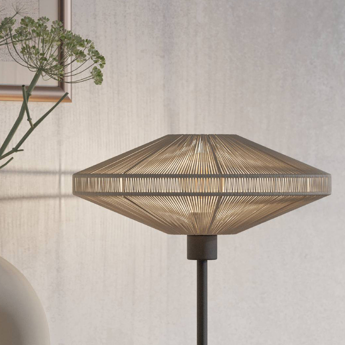 Close up of a table lamp with a woven shade and a dark base, next to a green plant