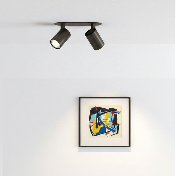 Two dark brown ceiling spotlights illuminating a framed abstract painting with blue, yellow, and red