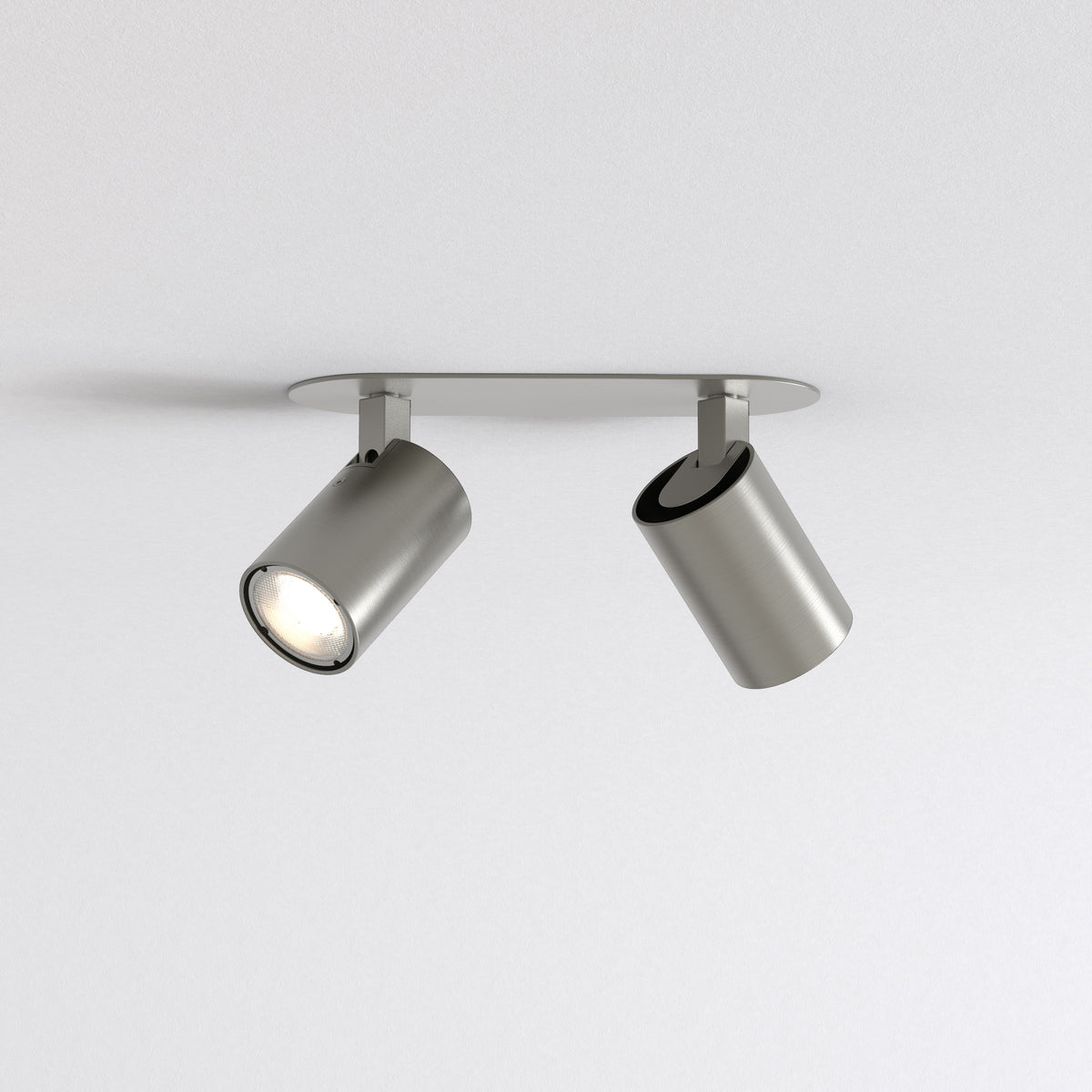 Two brushed metal ceiling spotlights on a white ceiling, one illuminated