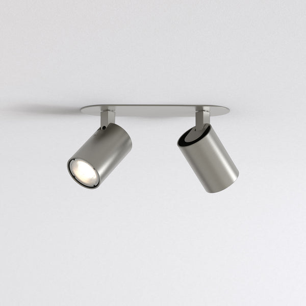 Two brushed metal ceiling spotlights on a white ceiling, one illuminated