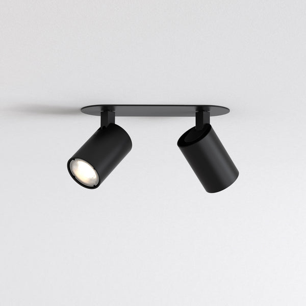 Two black cylindrical ceiling spotlights on a black rectangular base, one light is on and angled left