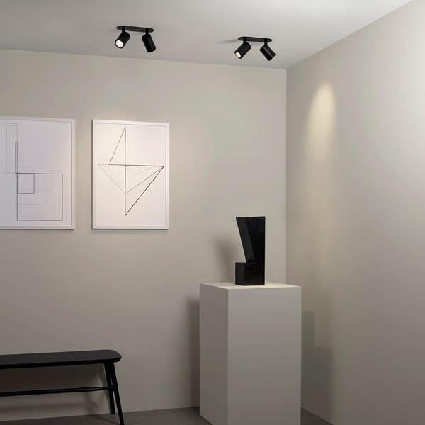 Two sets of black ceiling spotlights illuminate a modern art gallery with abstract wall art and a sculpture