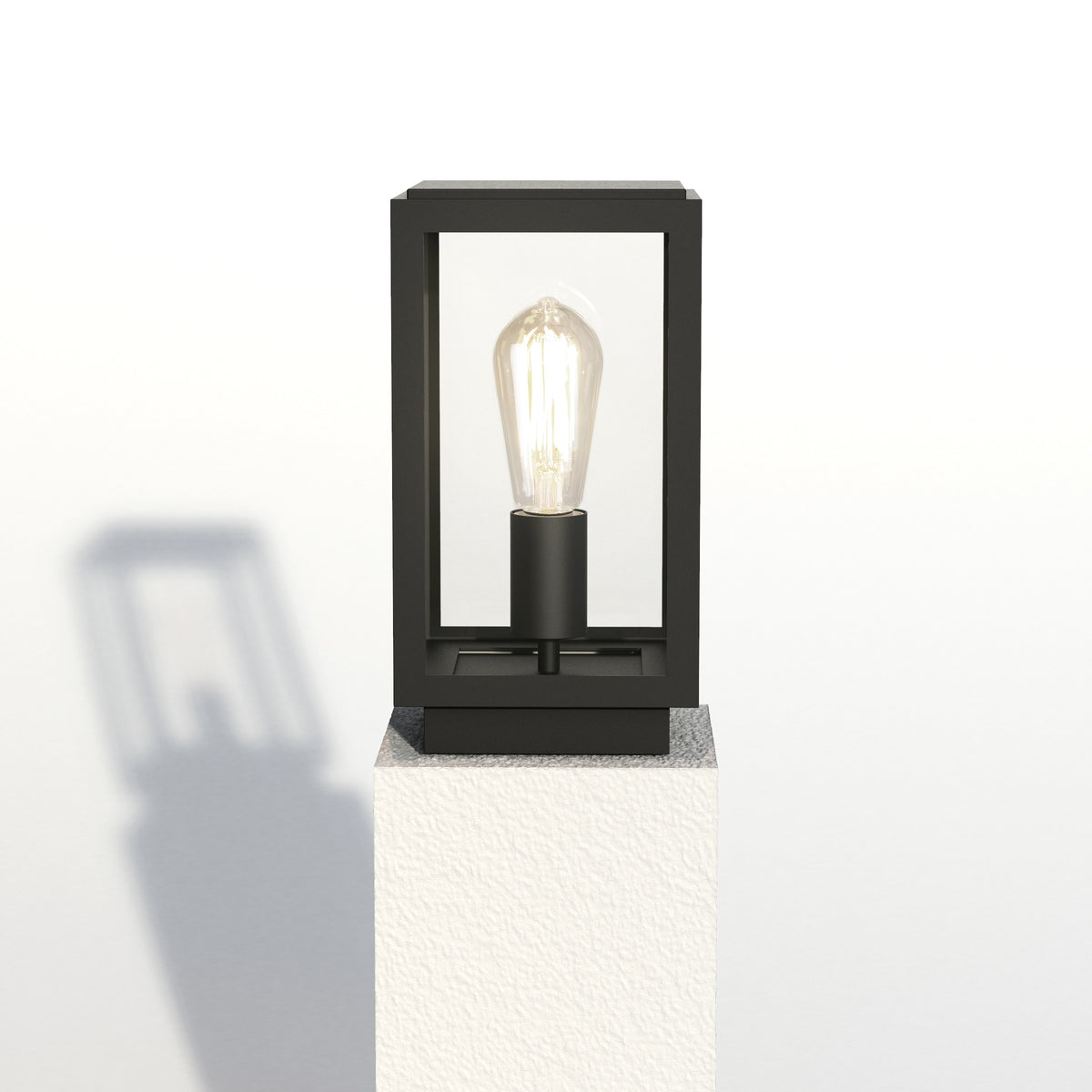 Black outdoor pillar light with a clear glass frame and an exposed Edison bulb on a white textured surface
