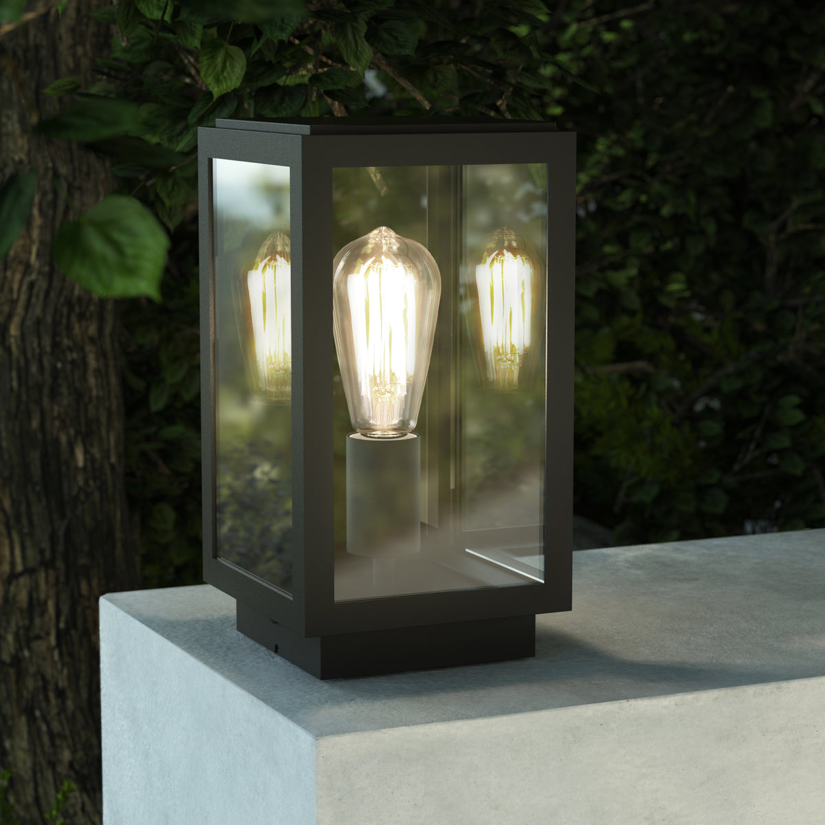 Black outdoor lantern with a clear glass casing and an exposed filament bulb, sitting on a concrete surface