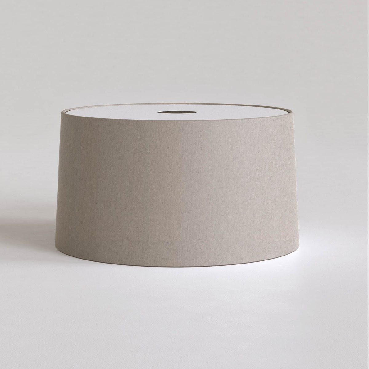 Cylindrical lamp shade in a light taupe fabric with a white top and a dark circular opening