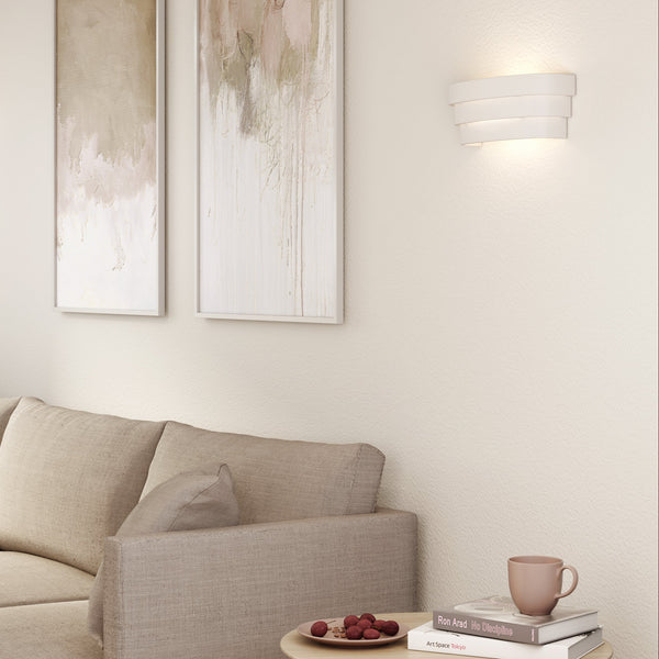 A beige sofa with two abstract paintings on the wall and a modern white wall light