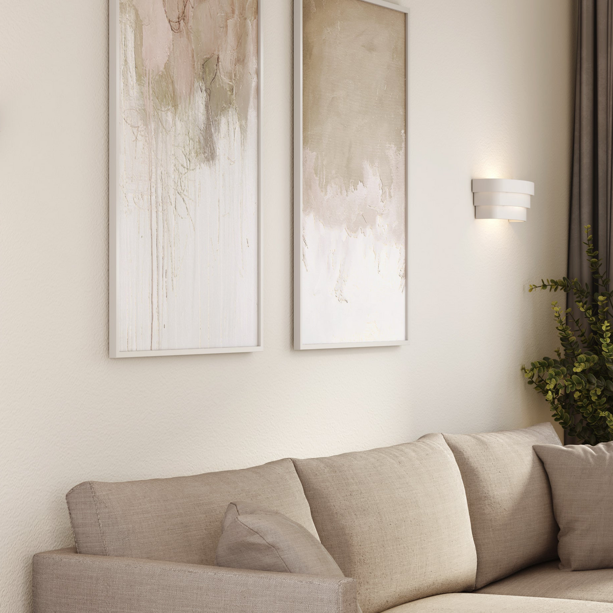Two abstract paintings on a wall above a beige sofa with a modern wall sconce and plant