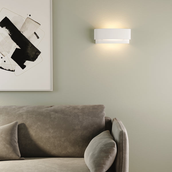White wall sconce illuminating a light green wall above a grey sofa with an abstract painting