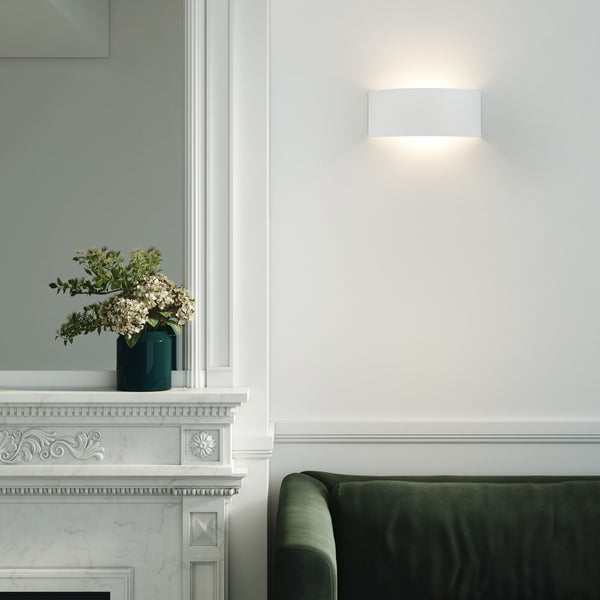 White wall sconce above a green velvet sofa, next to a marble fireplace with a teal vase of flowers