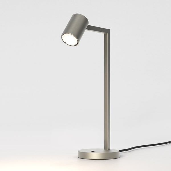 Brushed metal desk lamp with a cylindrical head and a rectangular arm, emitting a warm light
