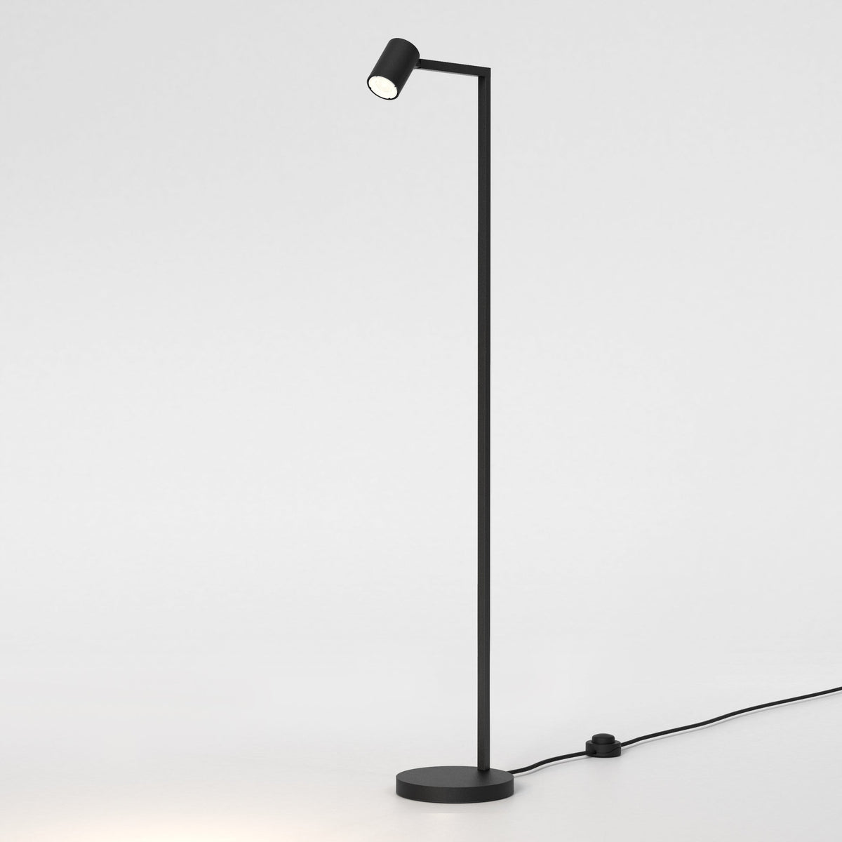 Black metal floor lamp with a round base and a small cylindrical light head, emitting a warm glow