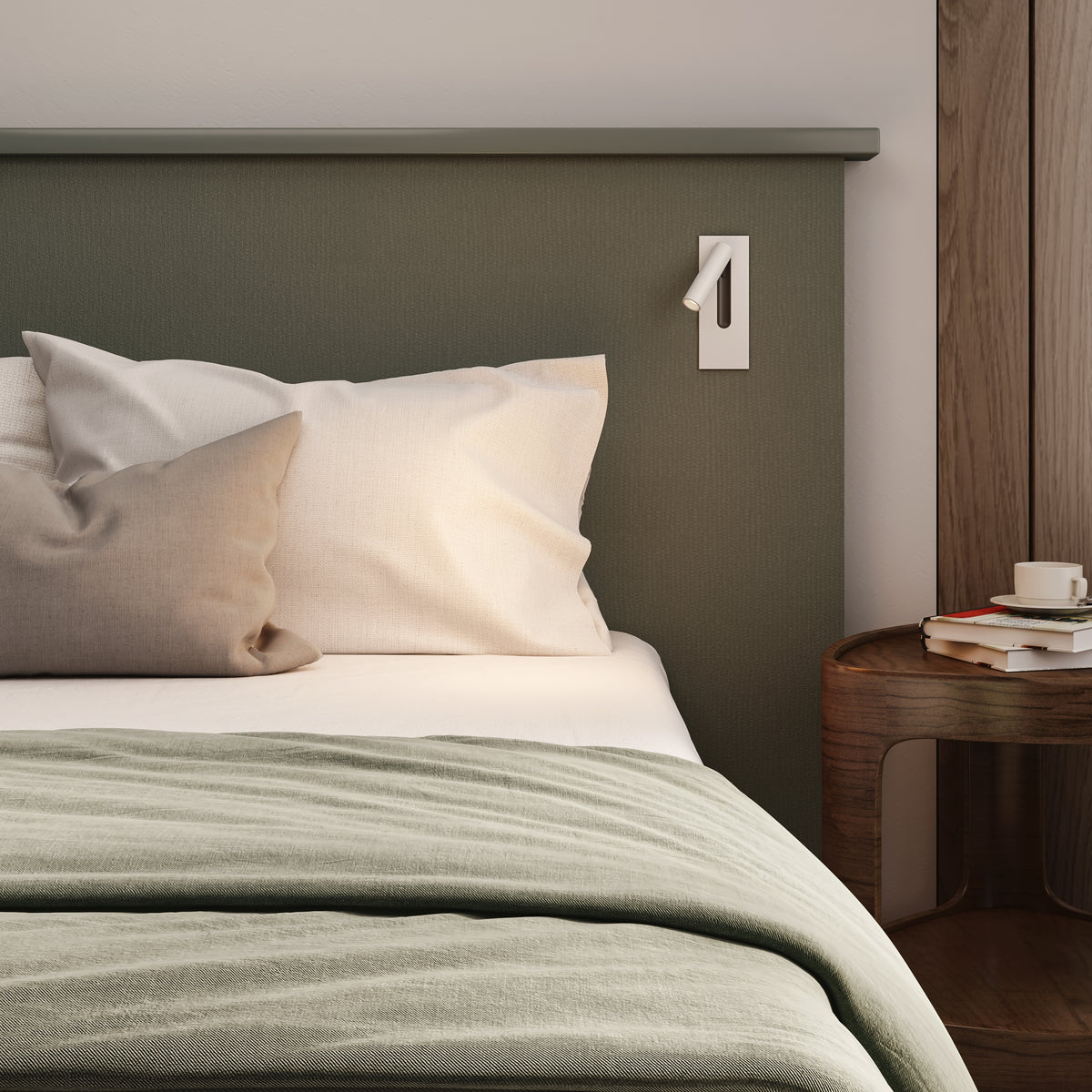 Bed with green headboard, white pillows, and a light green duvet. A wooden nightstand with books and a cup