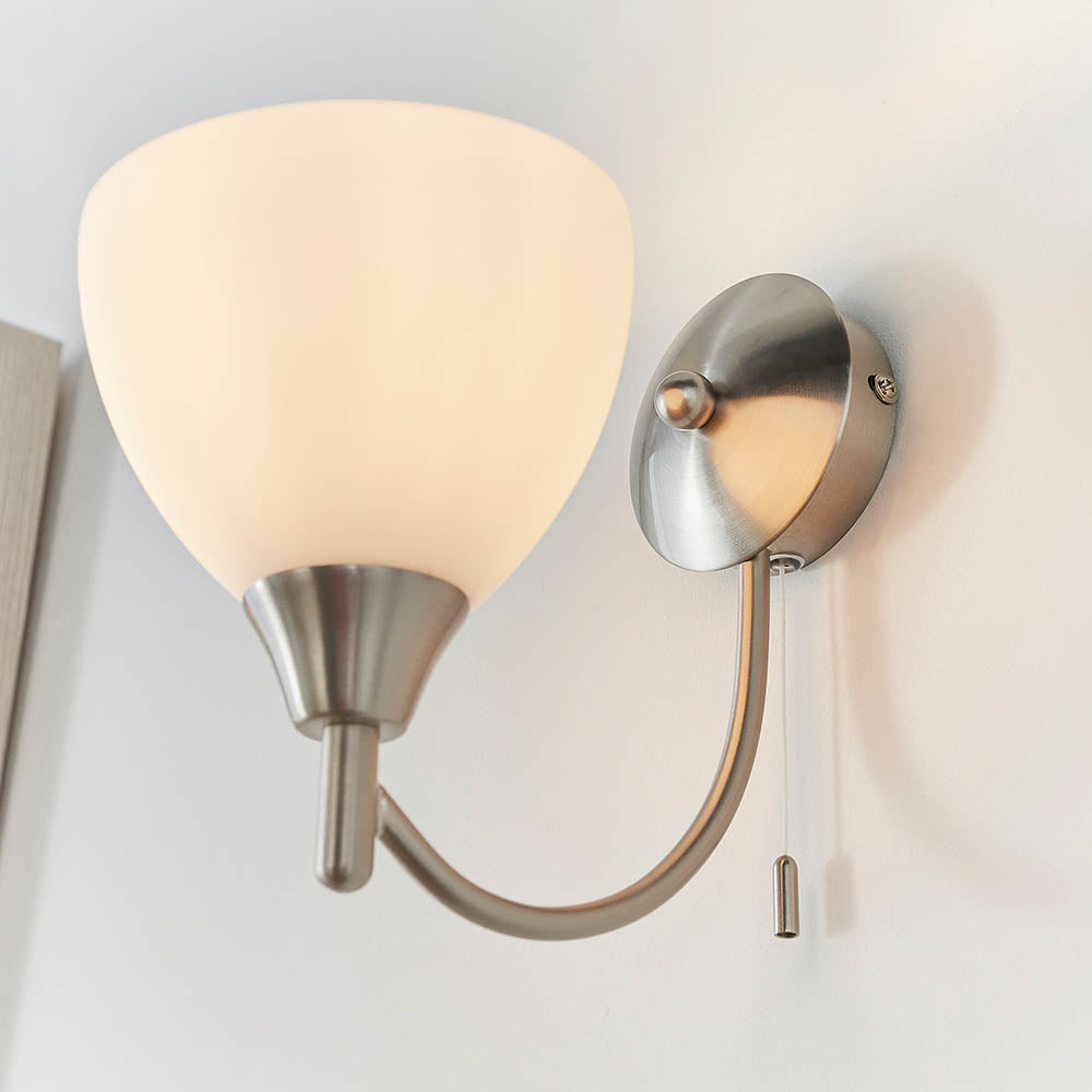 Brushed chrome wall light with a curved arm, an opaque white glass shade, and a pull cord switch.