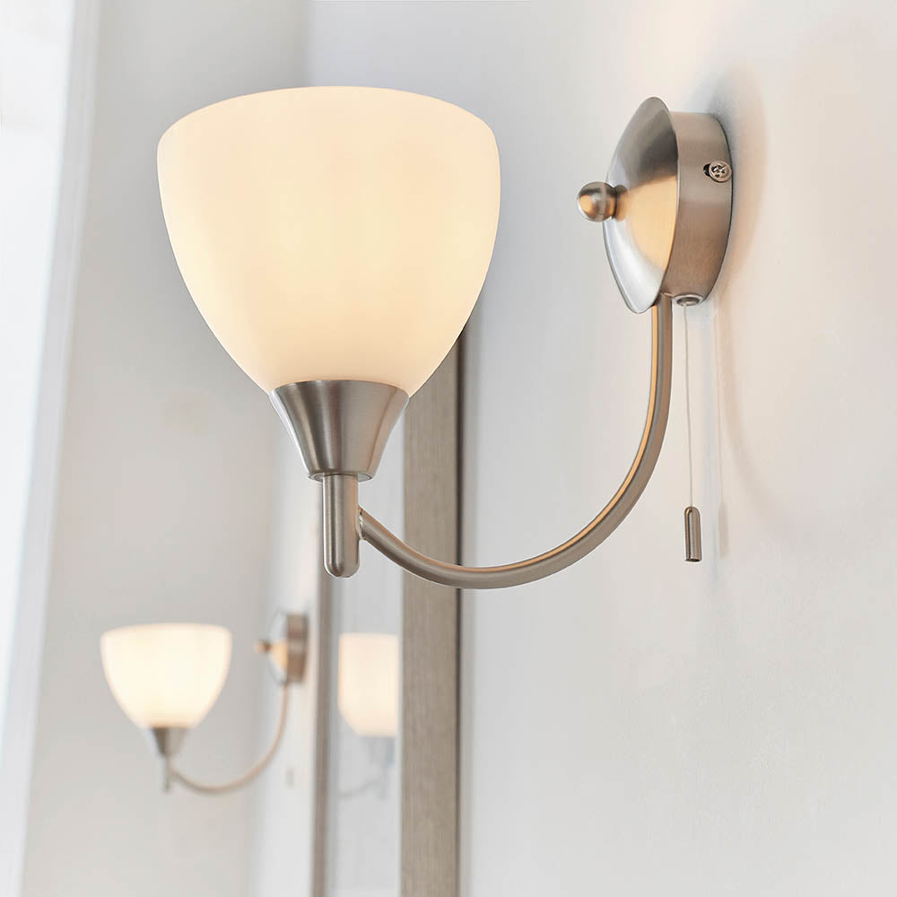 Brushed chrome wall light with a curved arm, an opaque white glass shade, and a pull cord switch, reflected in a mirror.