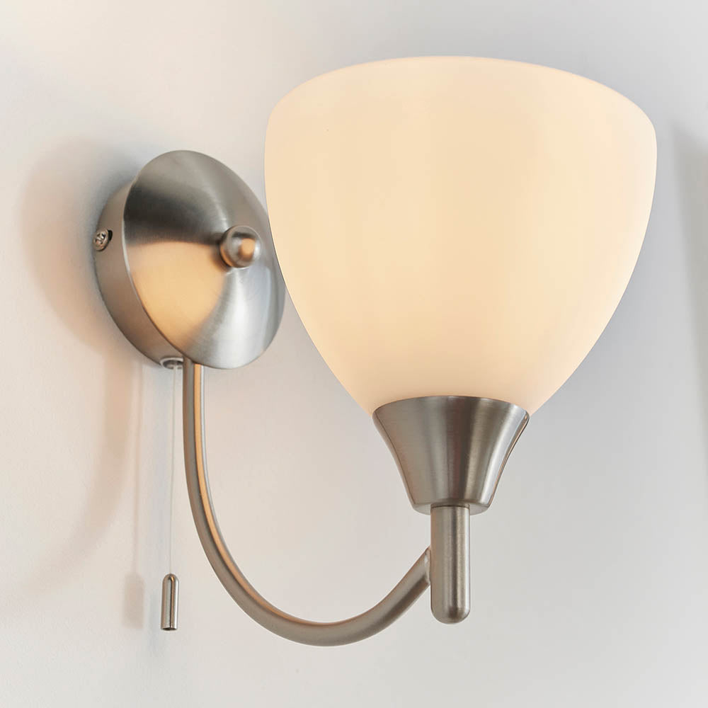 Brushed chrome wall light with a curved arm, an opaque white glass shade, and a pull cord switch.