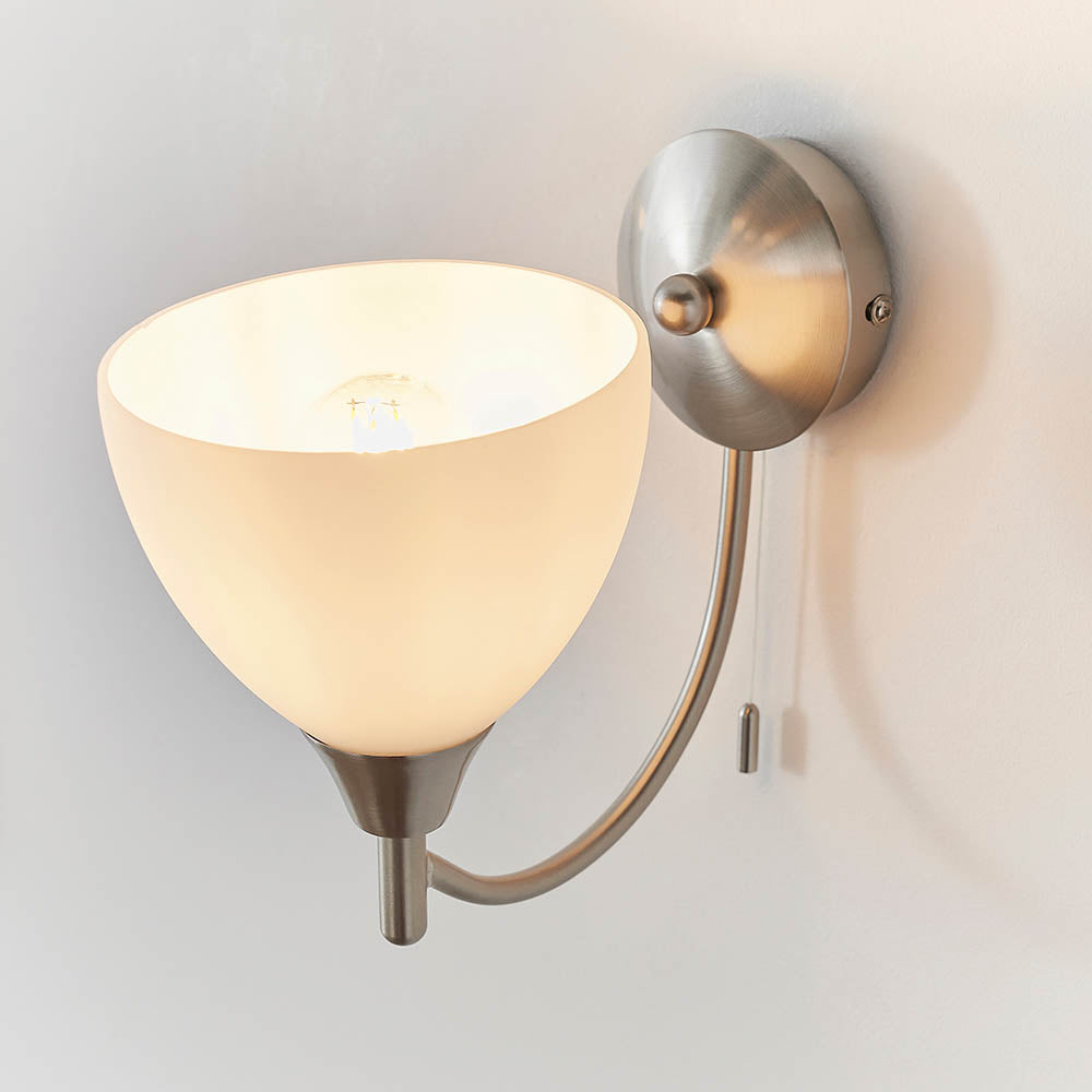 Brushed chrome wall light with a curved arm, an opaque white glass shade, and a pull cord switch.