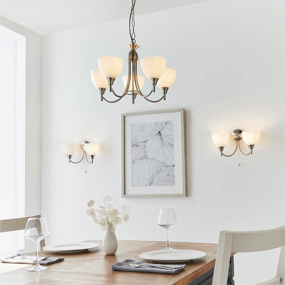 Dining room with a five-light chandelier and two matching two-light wall sconces, illuminating a wooden table.