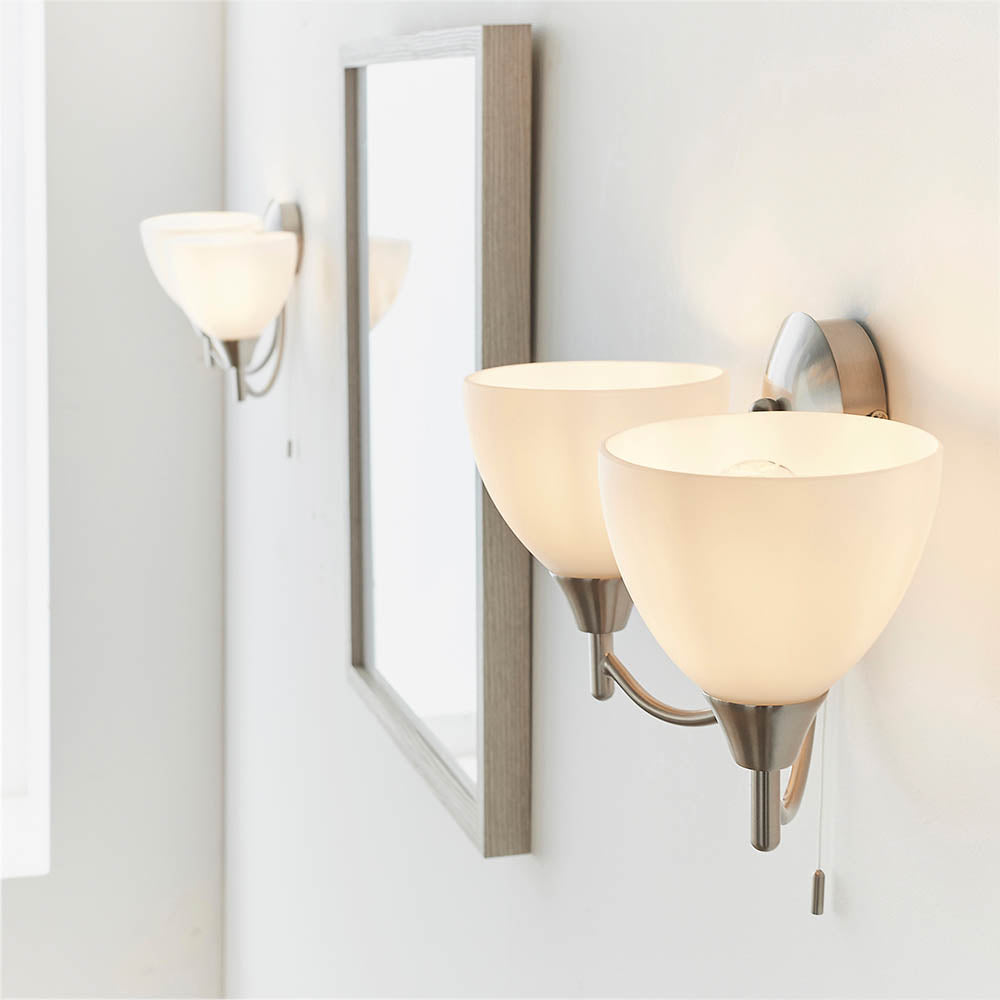 Two two-light wall sconces with brushed nickel finish and frosted glass shades, flanking a mirror.