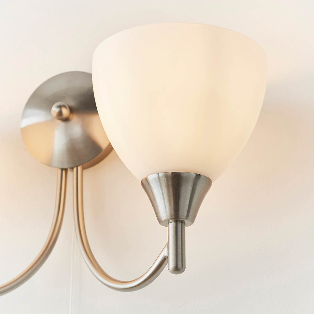Close-up of an illuminated frosted glass shade on a brushed nickel two-light wall sconce.