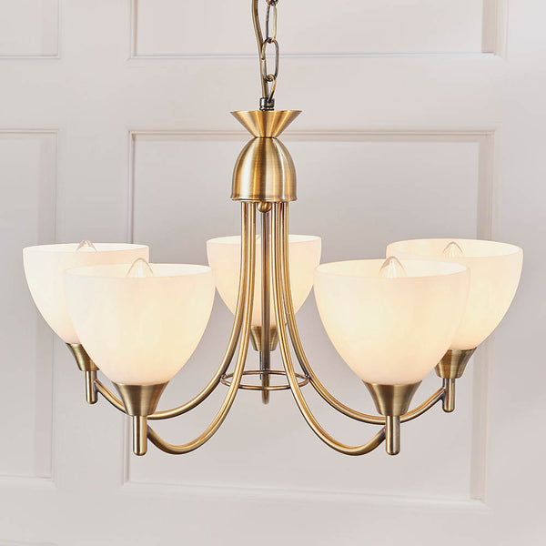 Close-up of a five-light antique brass chandelier with frosted glass shades against a white paneled wall.