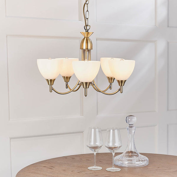 Five-light antique brass chandelier with frosted glass shades, two wine glasses, and a decanter on a wooden table.