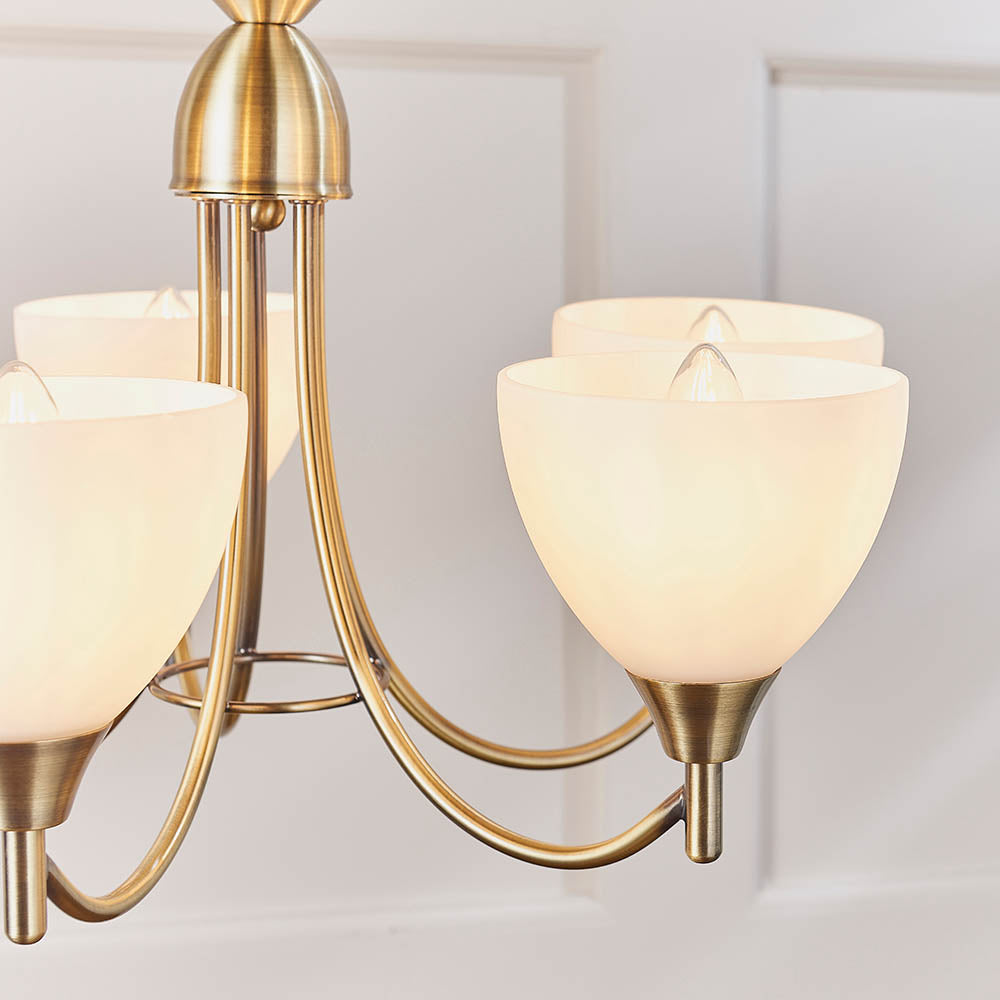 Close-up of the frosted glass shades and antique brass arms of a five-light chandelier.