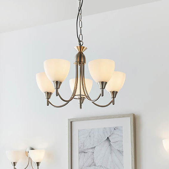 A five-arm chandelier with white glass shades and an antique brass finish hangs from a white ceiling.