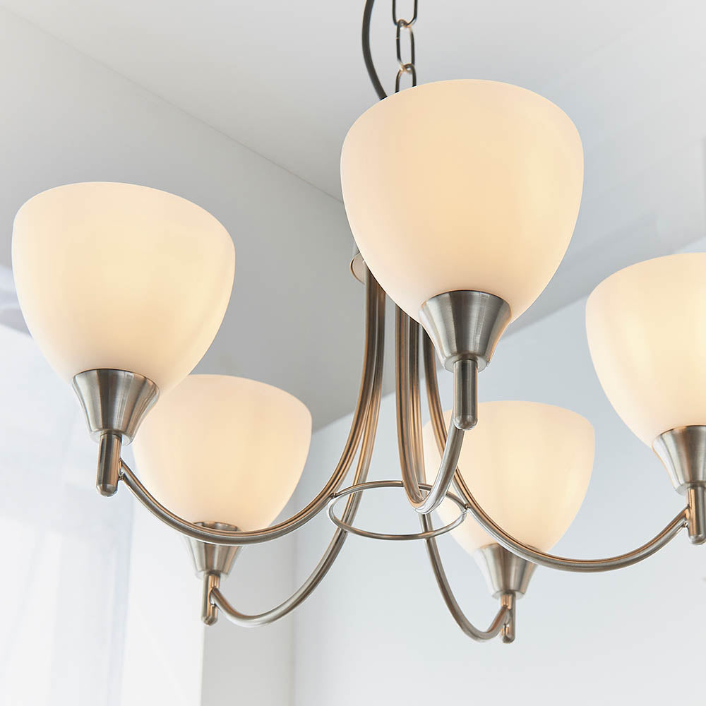 Close-up of a five-arm chandelier with white glass shades and a brushed chrome finish.