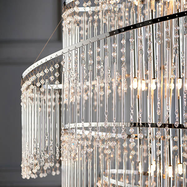 Close-up of a modern chandelier, showing tiers of clear crystal rods and small beads hanging from a silver frame.