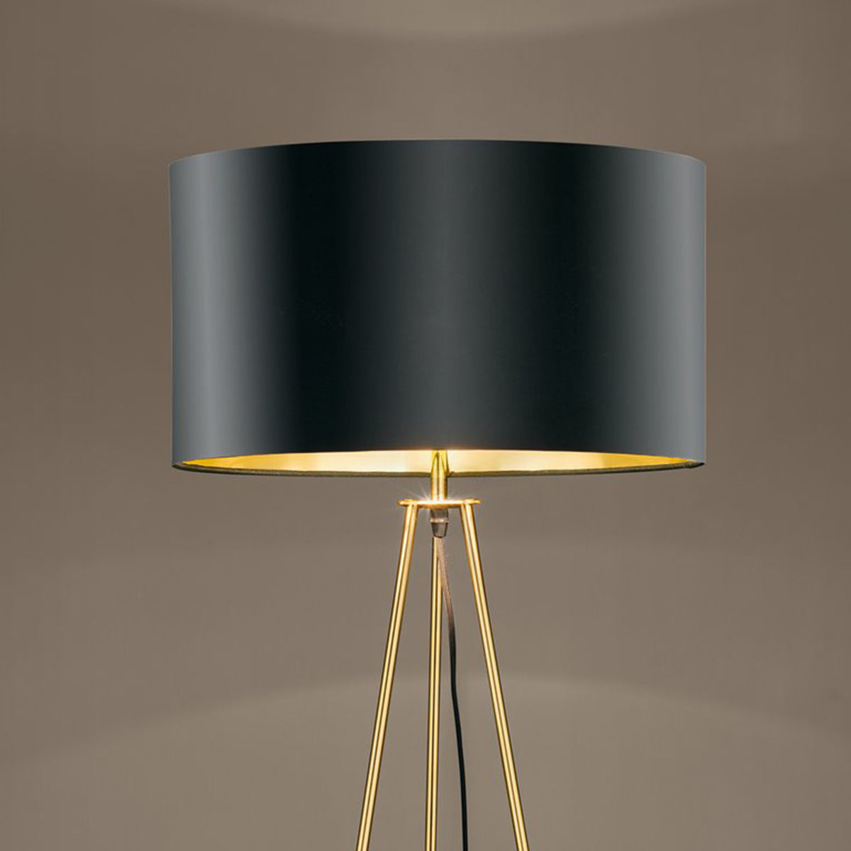 Modern floor lamp with a black cylindrical shade and a golden tripod base, emitting a warm glow.
