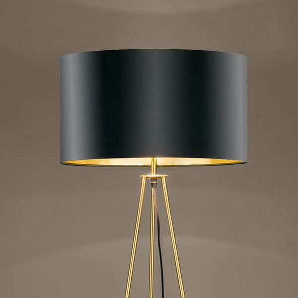 Modern floor lamp with a black cylindrical shade and a golden tripod base, emitting a warm glow.