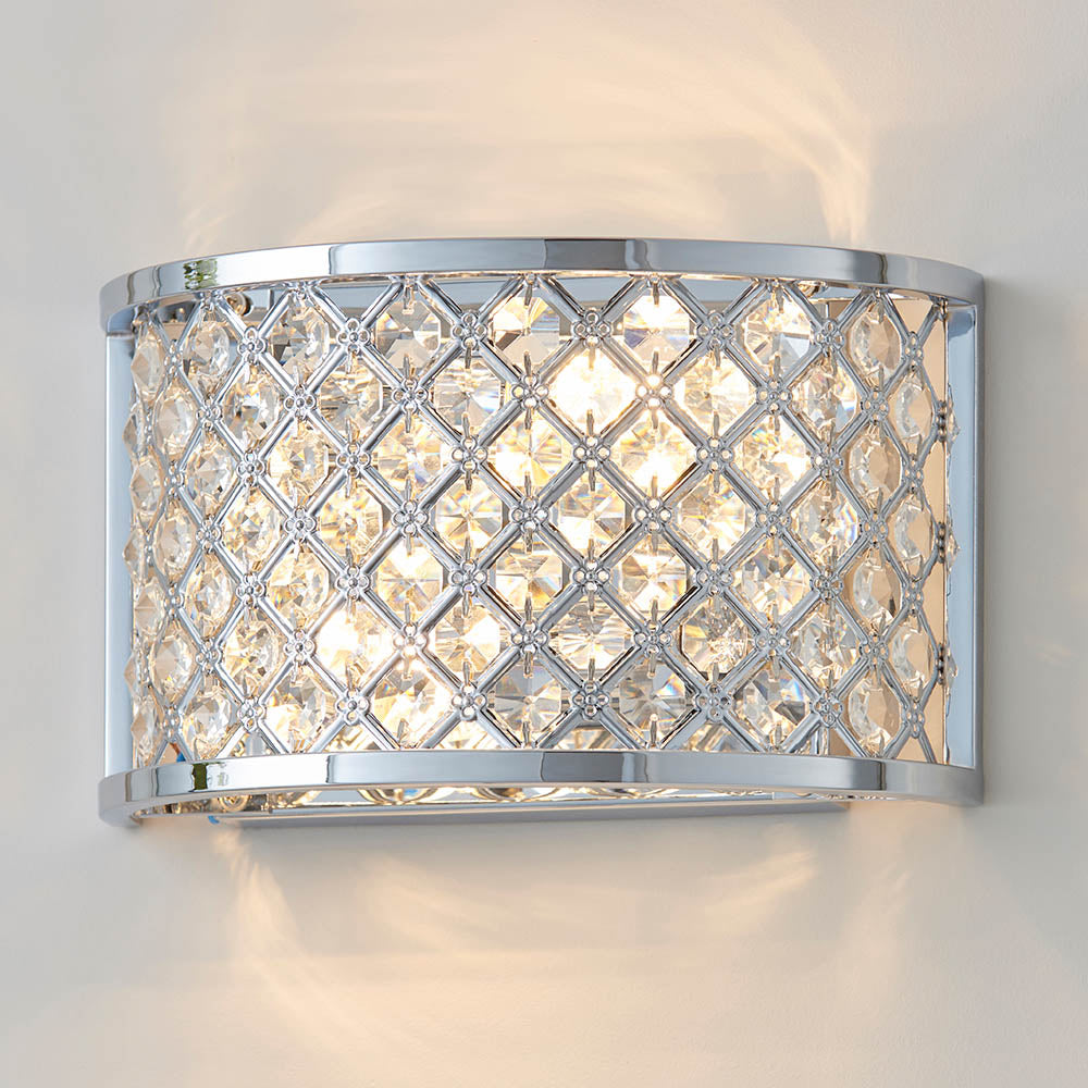 Chrome wall light with a curved crystal grid shade, casting light upwards and downwards on a white wall.