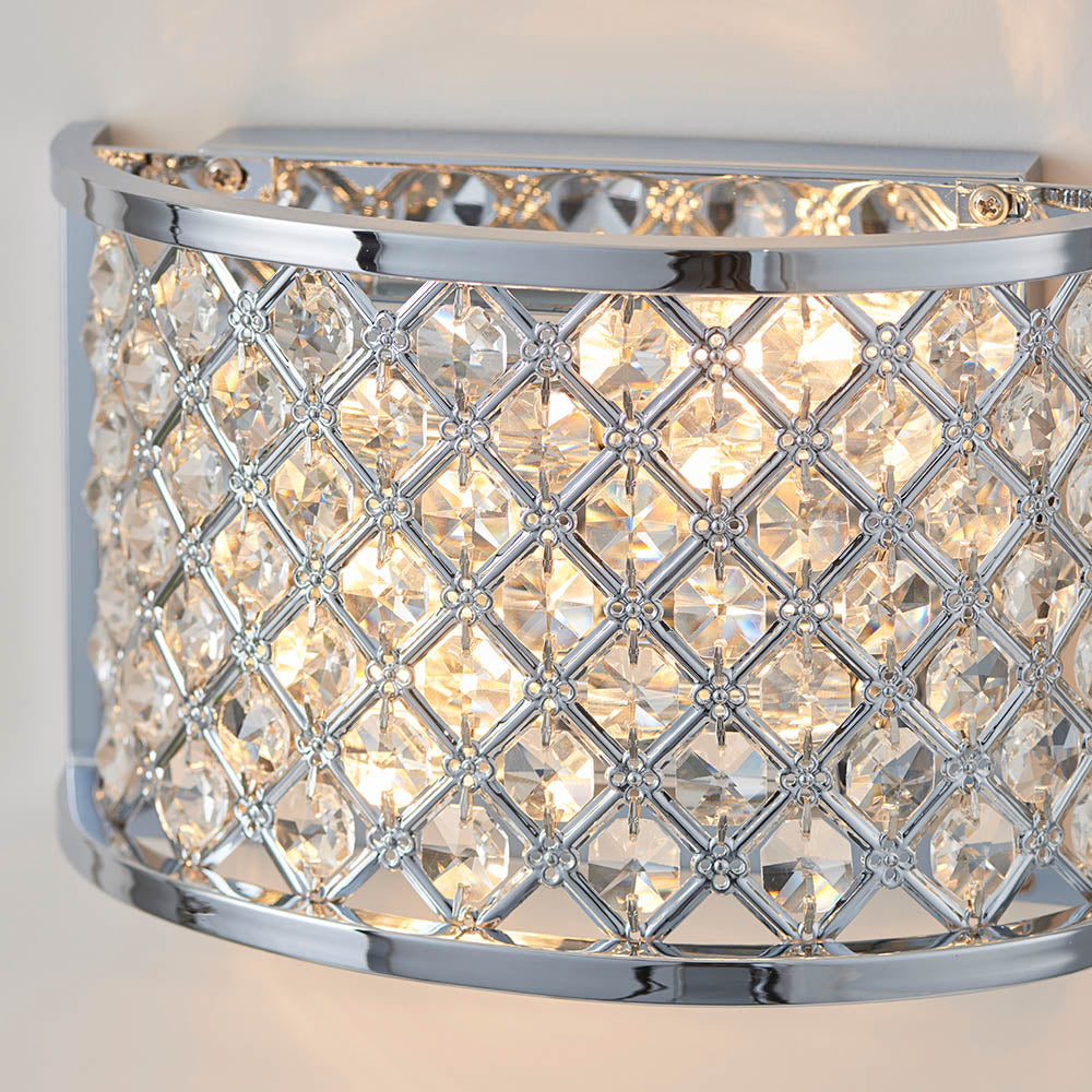 Close-up of a chrome wall light with a curved crystal grid shade, showing the illuminated crystals.