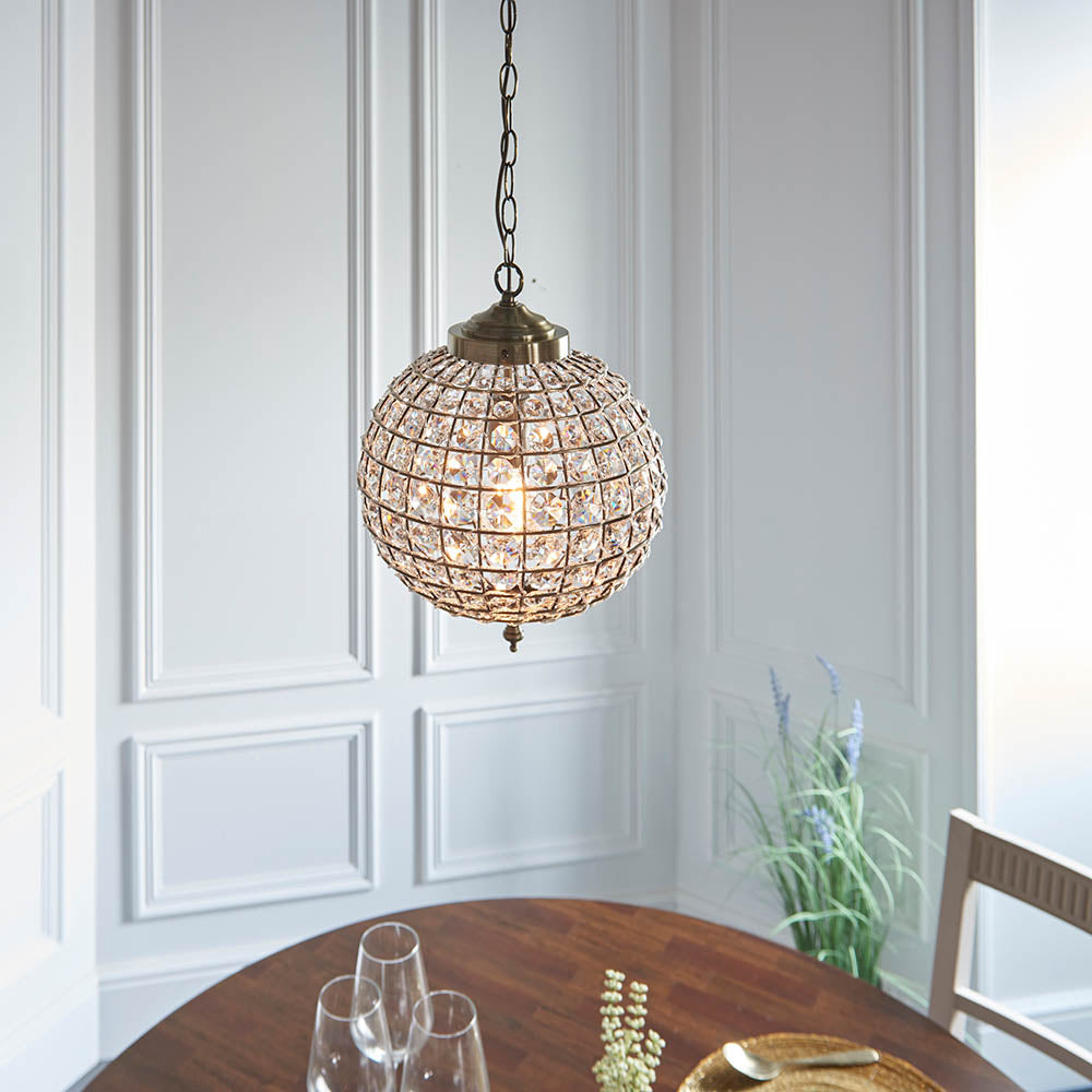 Crystal sphere pendant light hanging above a dining table in a room with white paneled walls.