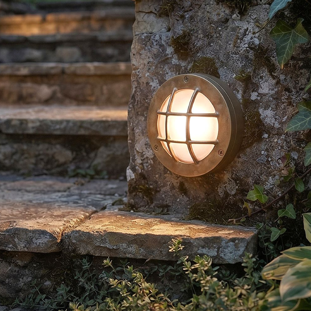 Round bulkhead wall light with metal cage mounted on a stone wall next to stone steps