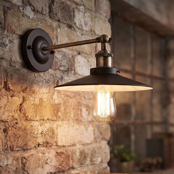 Industrial style wall sconce with a black metal shade and Edison bulb mounted on a brick wall