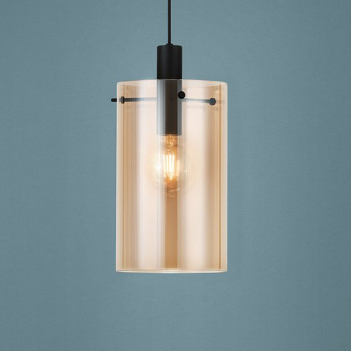 Modern cylindrical pendant light with an amber glass shade and a visible filament bulb.