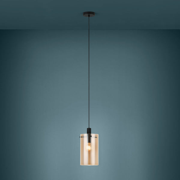 A modern pendant light with a cylindrical amber glass shade and a black fixture, hanging against a teal wall.