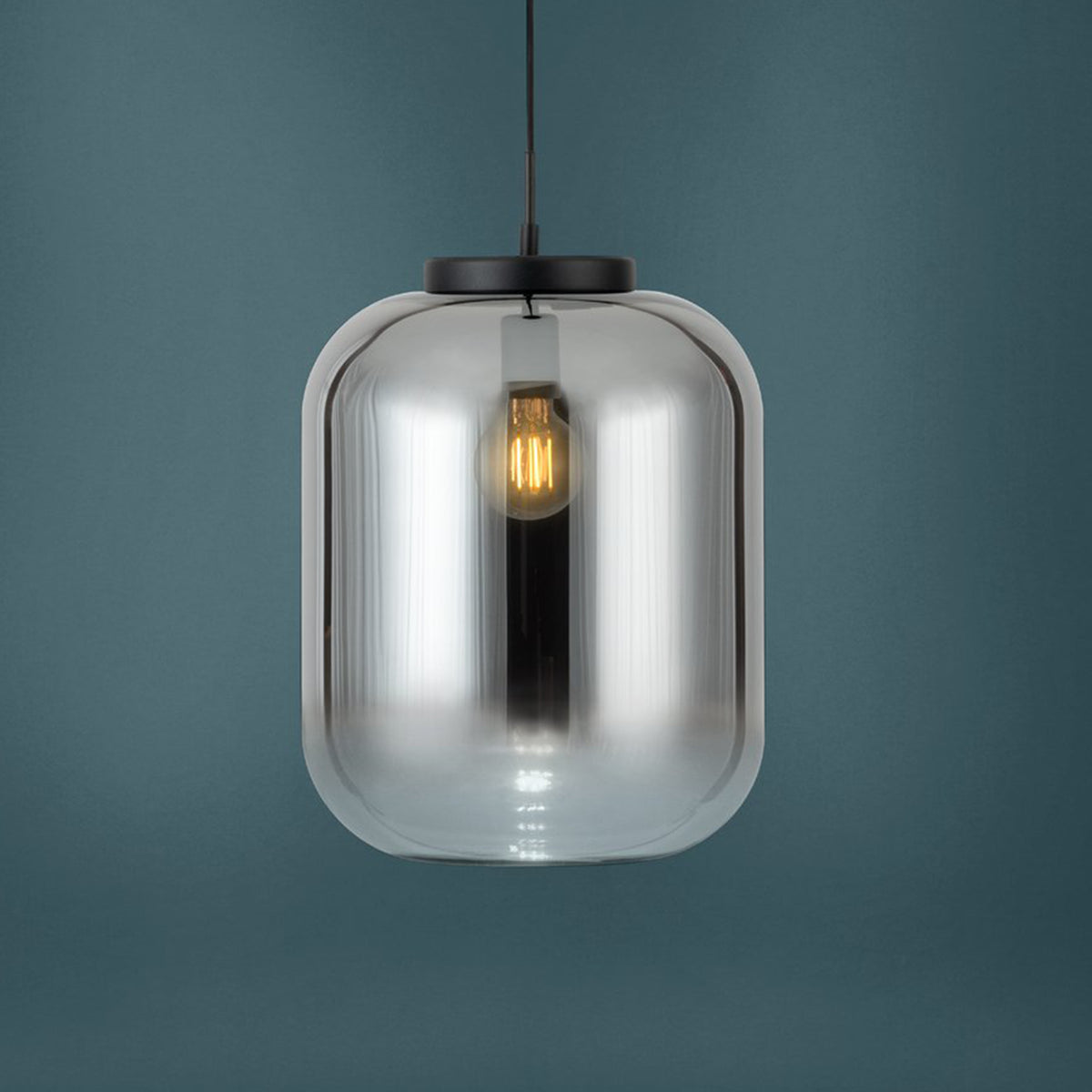 A modern pendant light with a clear, rounded glass shade and a visible filament bulb, hanging against a dark teal background.
