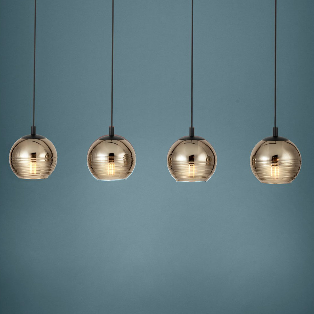 Four gold glass pendant lights with visible filaments hang against a blue-grey background. 