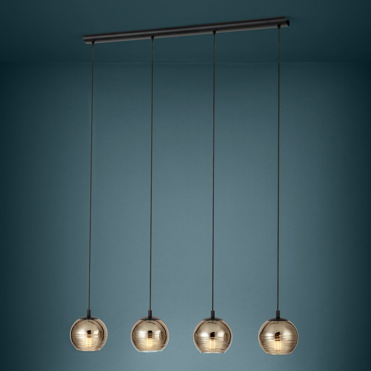 Four pendant lights with round, ribbed, amber glass shades hang from a black bar against a dark teal wall.