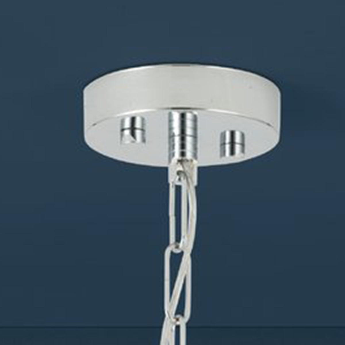 Close-up of a chrome ceiling rose with a hanging chain against a dark blue background.