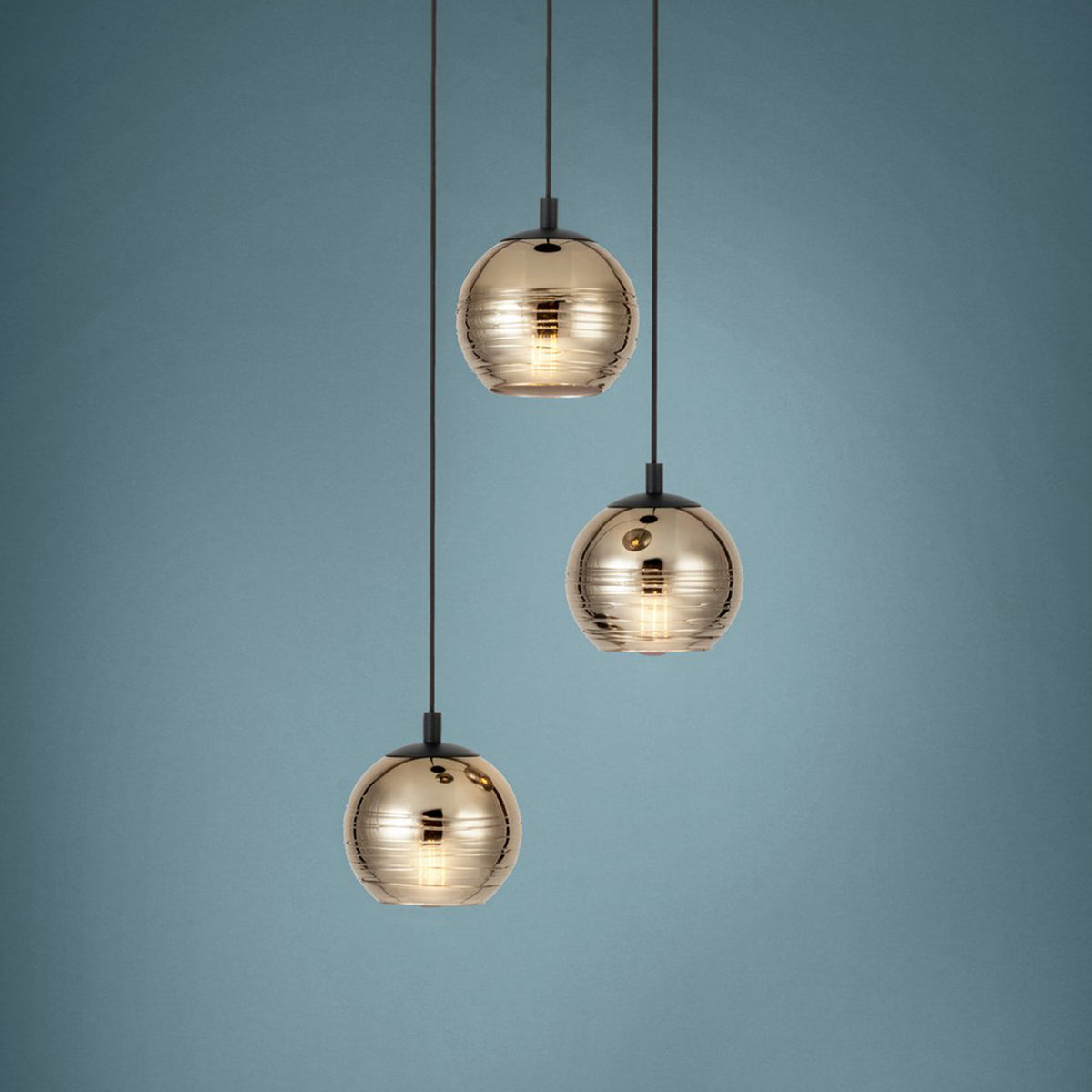 Three pendant lights with gold, ribbed, spherical shades hang against a blue wall. Each light glows warmly.