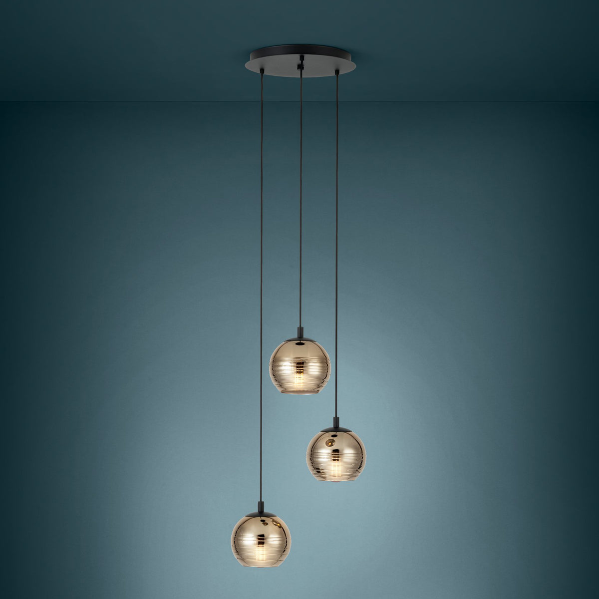 Three pendant lights with gold-tinted, ribbed glass globes hang from a black ceiling plate against a blue wall.