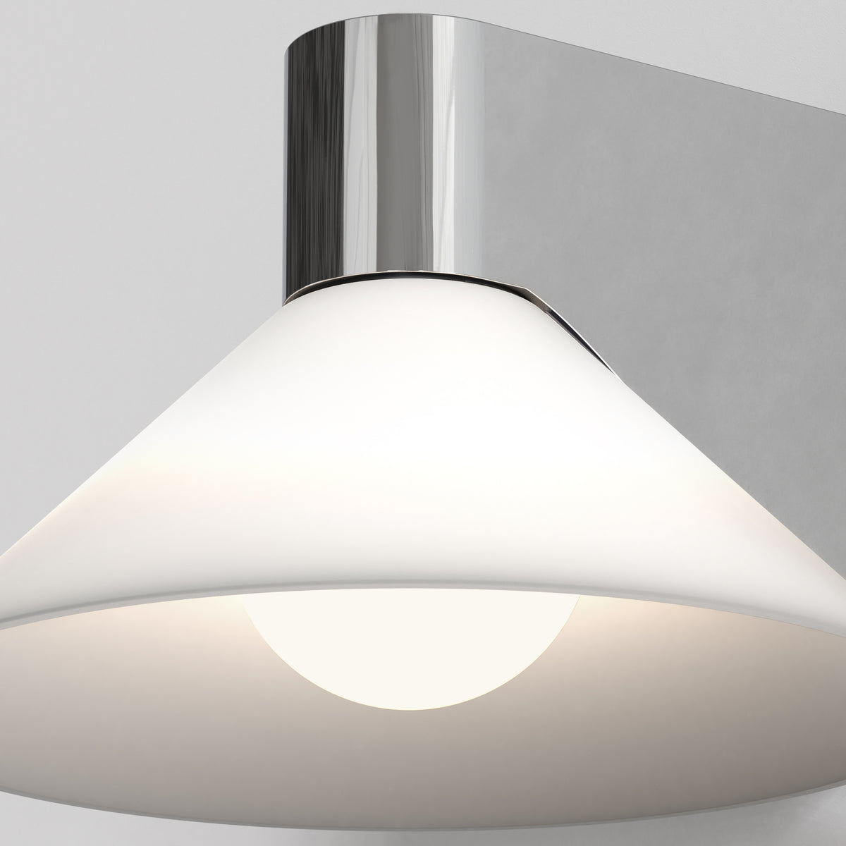 Close up of a white conical wall light with a chrome base, illuminating a white wall