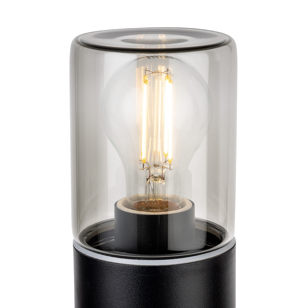 Close up of a black lamp base with a clear glass shade and an illuminated filament bulb inside