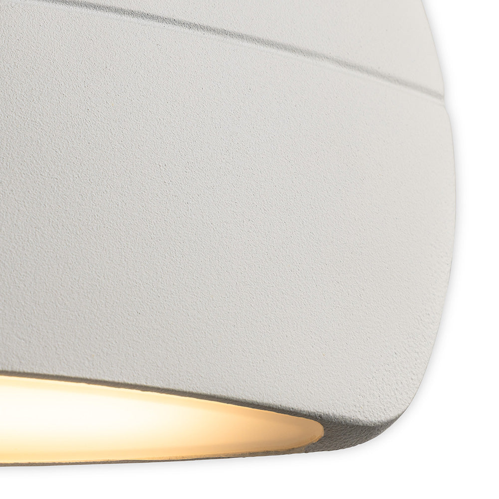 Close up of a white textured wall light with a warm glow from the bottom