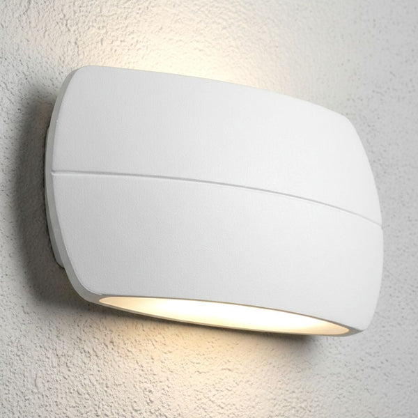 White curved wall light with a horizontal groove, emitting warm light upwards and downwards on a textured wall