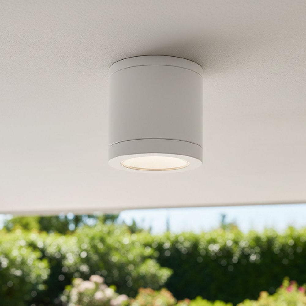 White cylindrical ceiling light fixture with a warm glow, mounted on a white ceiling outdoors