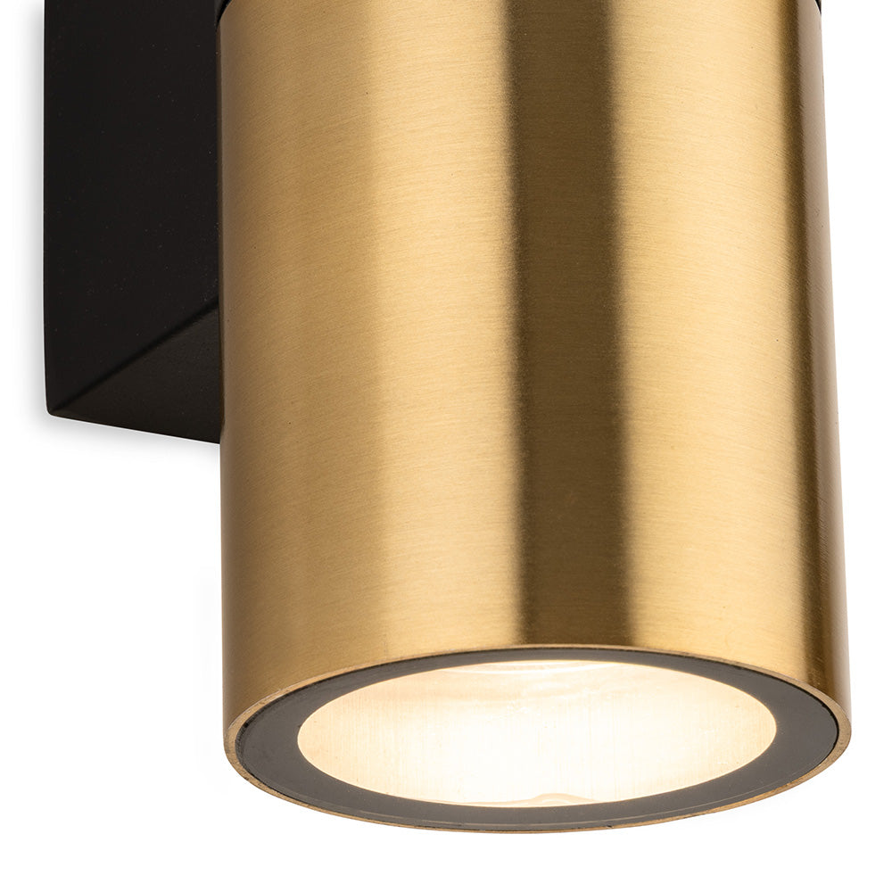 Close up of a brass cylindrical wall light with a black base, shining downwards